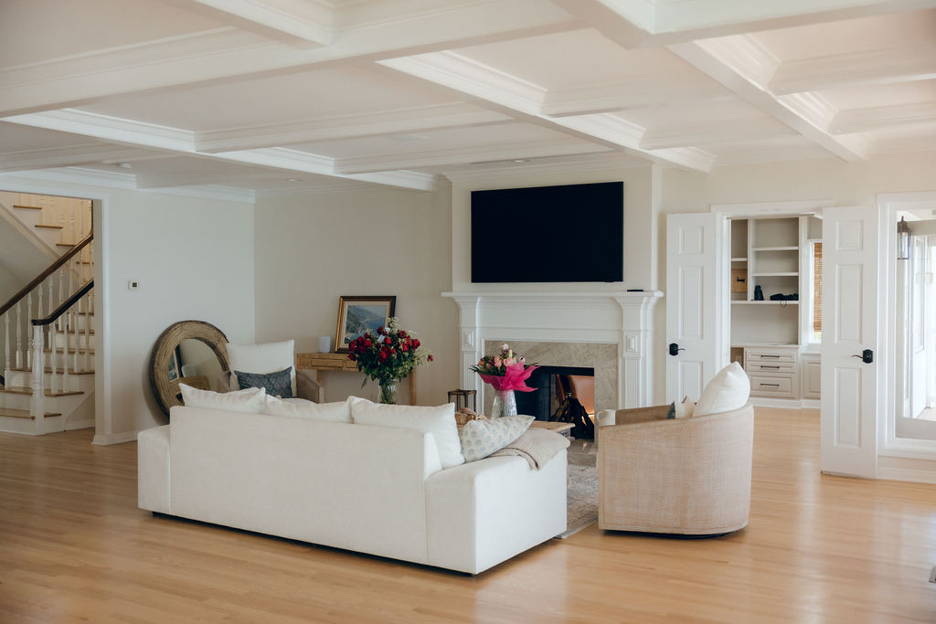 Light-filled living room with white seating, warm wood floors, and a coffered ceiling